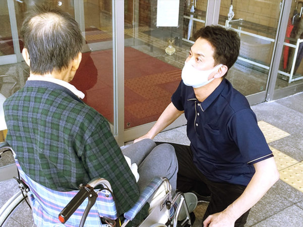 スタッフが高齢入居者に対応している介護施設の玄関・受付エリア